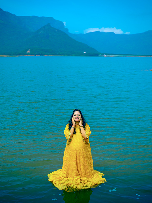 Expectant mother in vibrant attire stands peacefully by the water in Coimbatore, a beautiful moment by Bee Bee Videos' maternity photography.