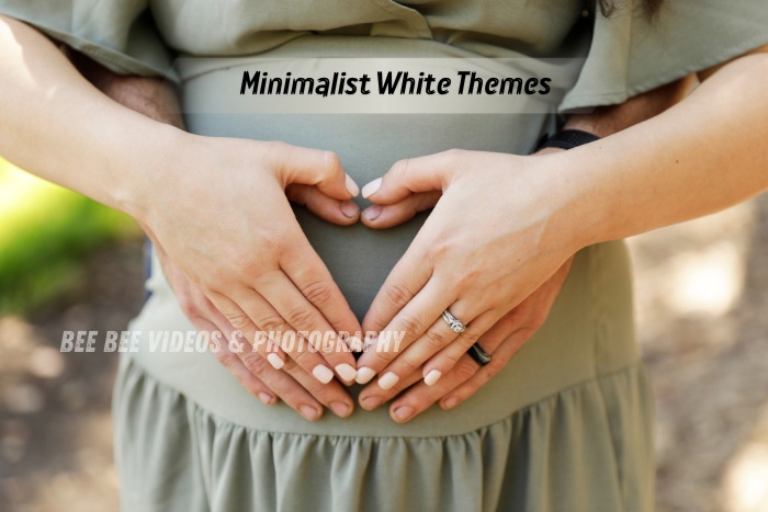 Close-up maternity photo showing a couple forming a heart shape on a baby bump, styled in minimalist tones