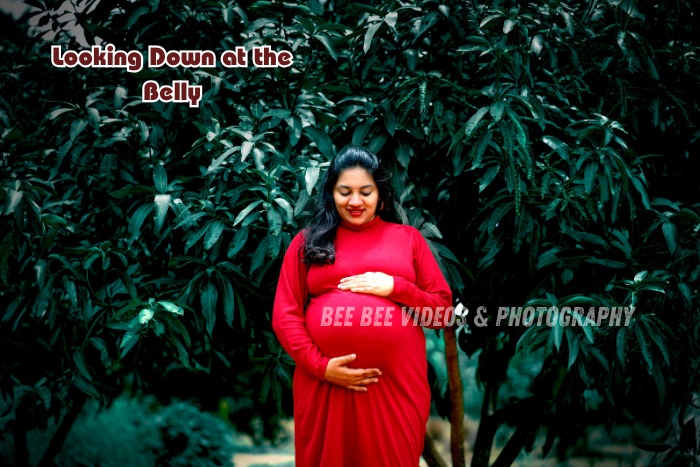Maternity photoshoot in Coimbatore featuring a mom-to-be in a red gown gently looking down at her baby bump